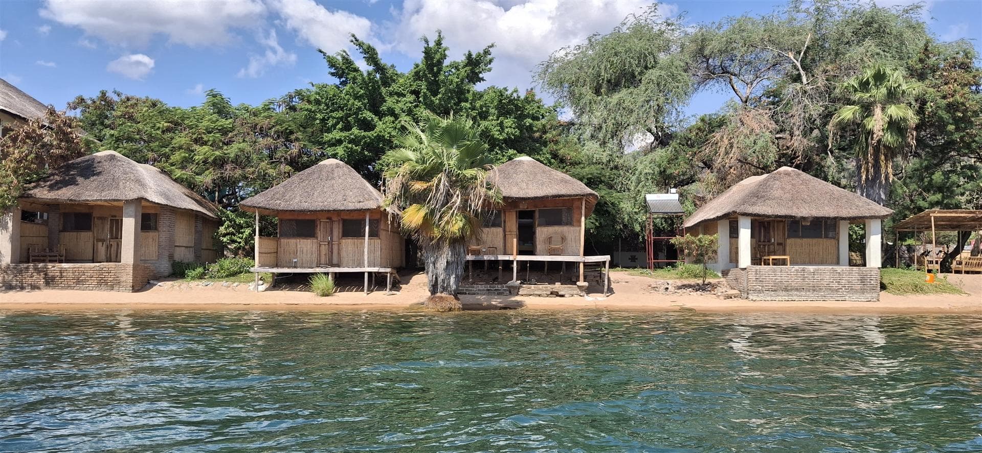 Grass-thatched chalets on the waterline with a palm tree standing in the lake