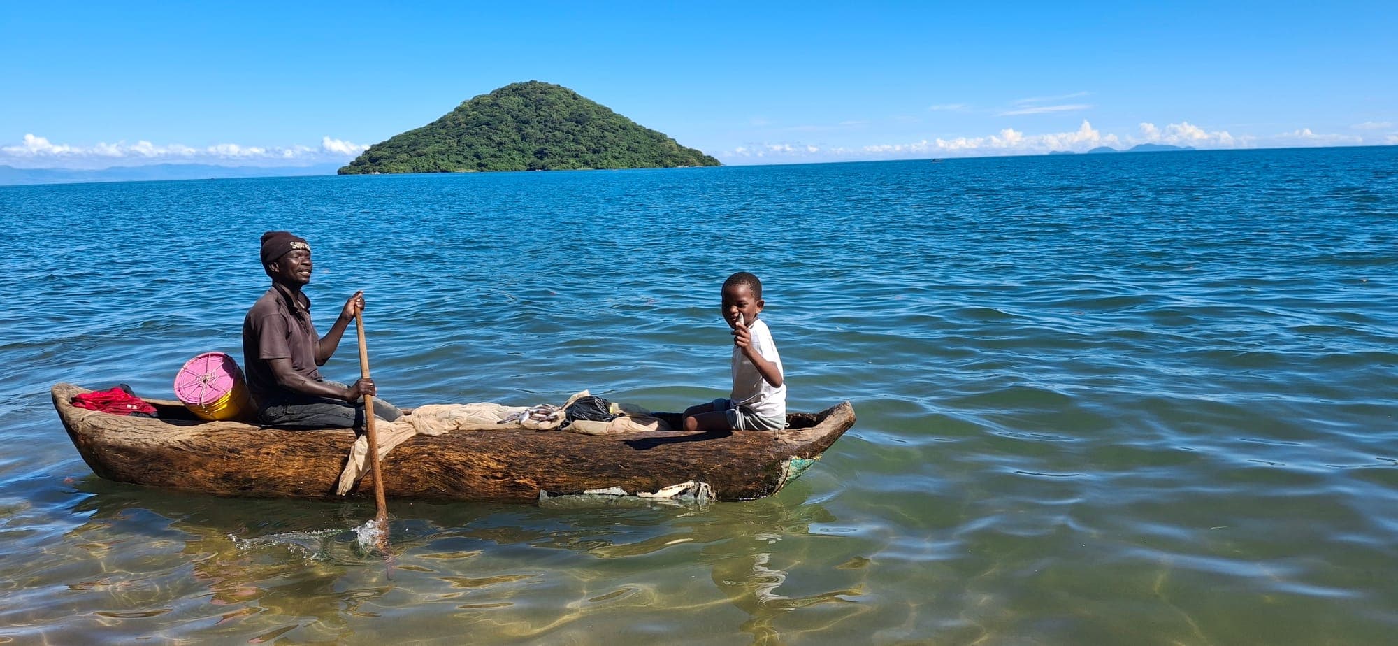 A fisherman and his son paddling a dugout canoe with the island behind